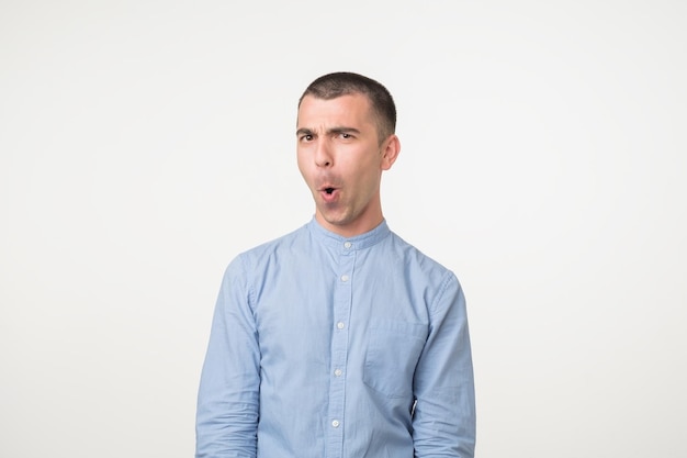 Shocked face of caucasian young man in blue shirt on grey background