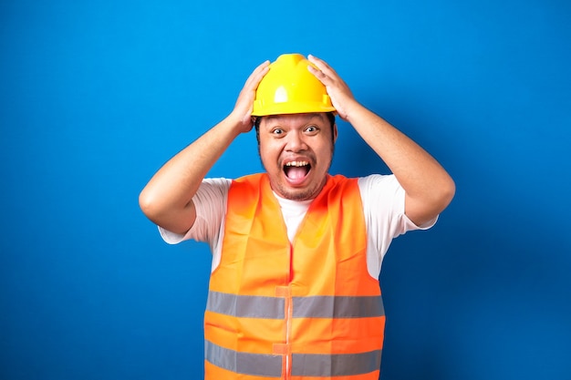 Shocked fat asian builder worker man is holding his hands on his head with wide open mouth isolated.