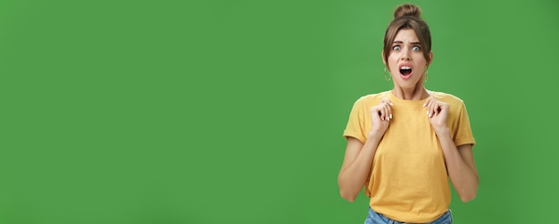 Shocked feminine glamour woman with combed hair in yellow tshirt frowning gasping with opened mouth