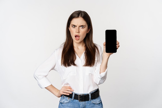 Shocked and frustrated woman showing mobile phone screen app smartphone application looking insulted...