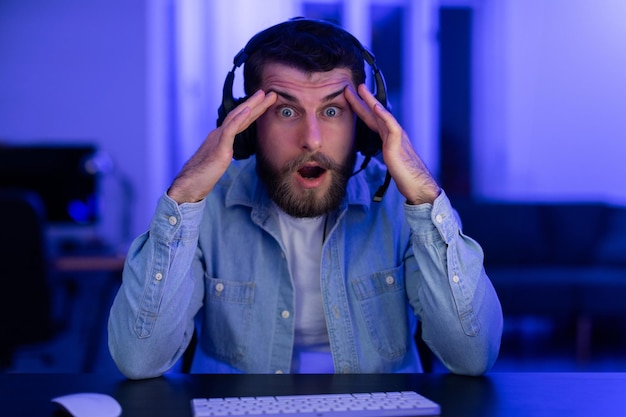 Shocked gamer with hands on head at desk