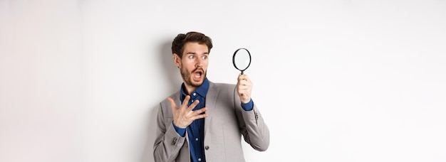 Shocked guy look through mafnifying glass with startled face gasping and holding hand on chest scare