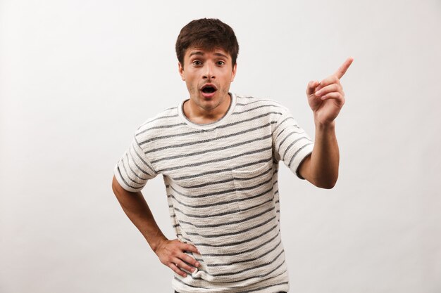 Shocked handsome man standing isolated on white wall pointing.