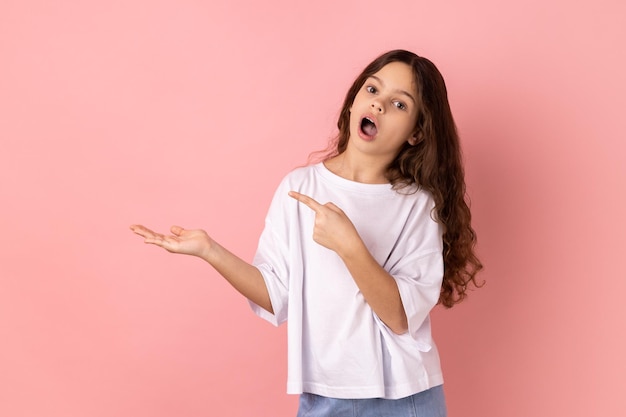 Shocked little girl presenting copy space on palm showing empty place for commercial text or goods