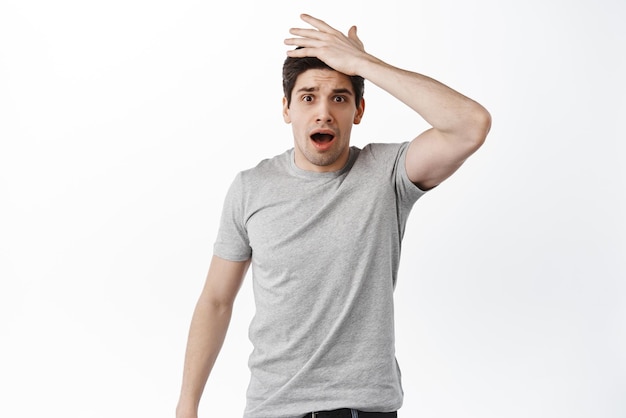 Shocked man forgot remember something slap forehead and gasp at camera standing forgetful against white background Copy space