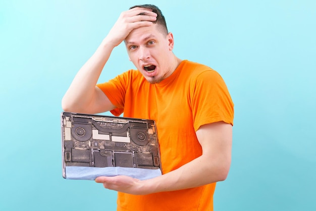 shocked man holding his head and holding an opened dirty and dusty laptop on a blue. Overheating