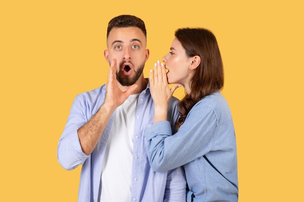 Photo shocked man looking at camera while woman whispering secret