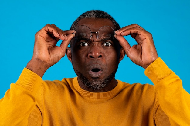 Shocked mature african american man removing eyeglasses on blue