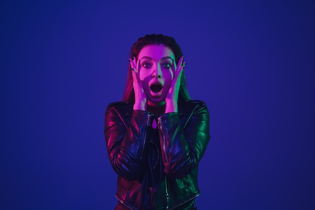 Shocked, scared. Caucasian woman's portrait isolated on blue studio background in neon light. Beautiful female model. Concept of human emotions, facial expression, sales, ad. Trendy colors.