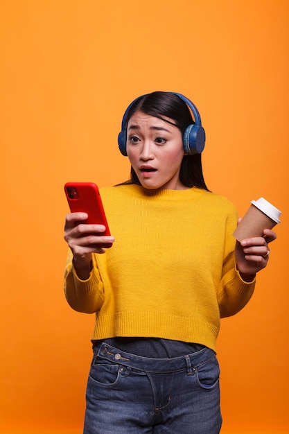 Shocked speechless young adult woman reacting in fear while reading tragic news on smartphone device. Frightened astonished asian person using mobile cellphone while left stunned.