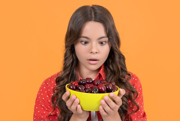 Shocked teen girl hold cherry bowl on yellow background