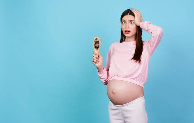 Shocked upset young pretty scared pregnant girl holds a comb in her hand