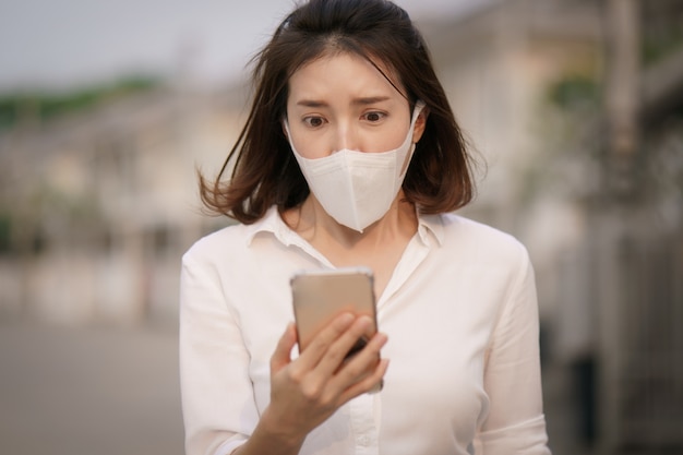 Shocked woman wearing protective mask and uses smart phone, worried about the news of the corona virus