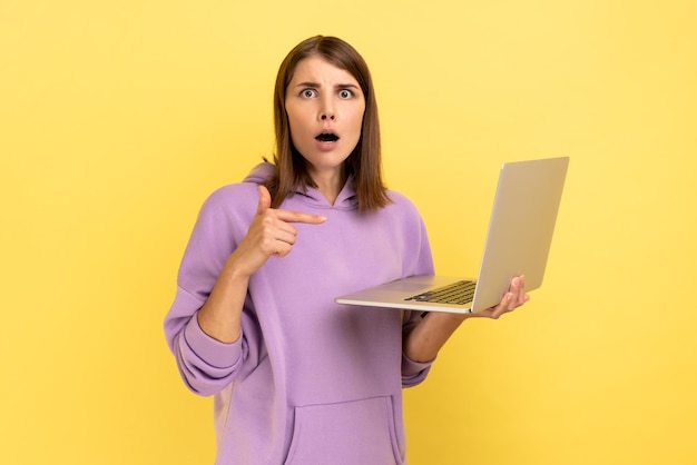 Shocked young adult woman working on laptop compute looking at camera and pointing at display