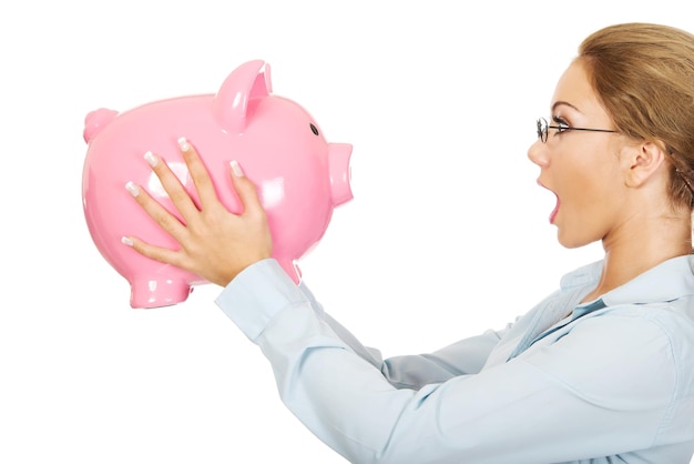 Photo shocked young businesswoman holding pink piggy bank against white background