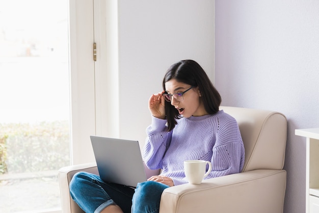 Shocked young ethnicity woman looking in computer and fixing her glasses. Lockdown news, online shocking low price.