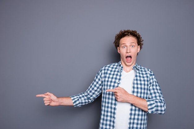 Shocked young man in casual checkered shirt pointing two fingers aside