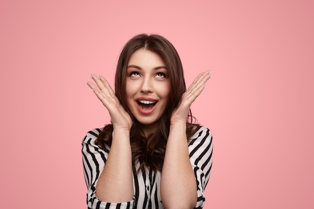 Shocked young woman looking up in pink studio