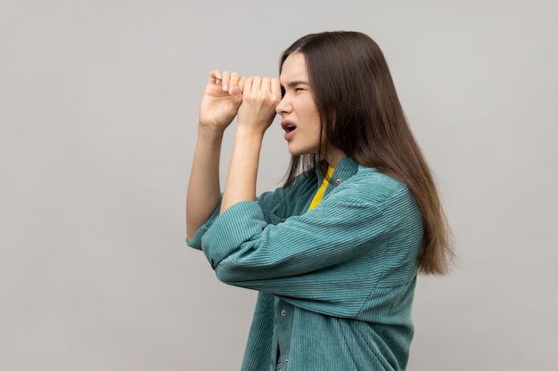 Shocked young woman standing with hands on eye monocular gesture looking away with surprised face