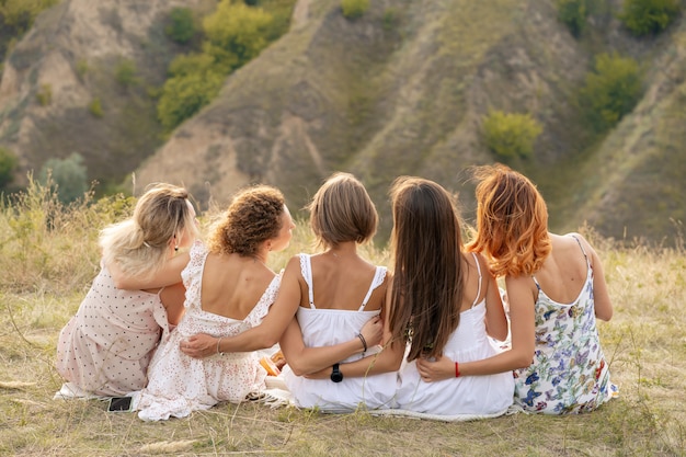 Shoot from back. The company of female friends having fun, hugs each other and enjoy hills landscape