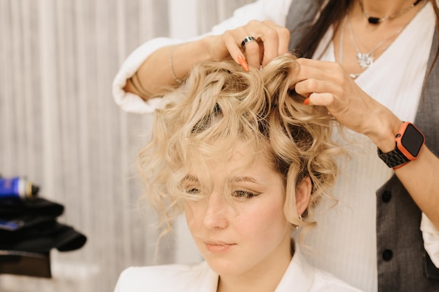 Shooting in a beauty salon A hair stylist makes a hairstyle for a young darkhaired girl with the help of a hair styler