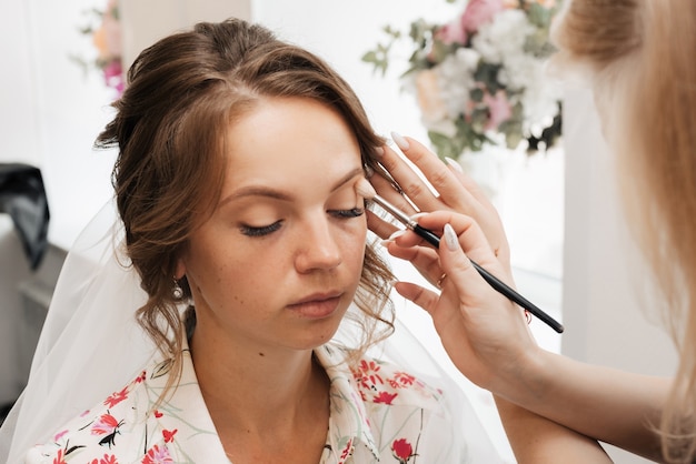 Shooting in a beauty salon. makeup artist applies makeup to a young beautiful girl bride.