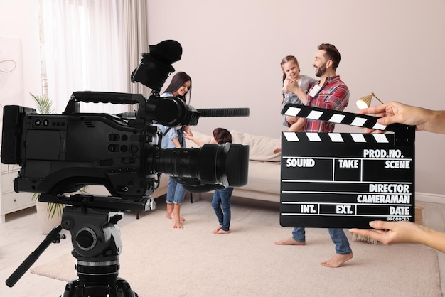 Shooting movie Second assistant camera holding clapperboard near video camera in front of happy family actors at home film set