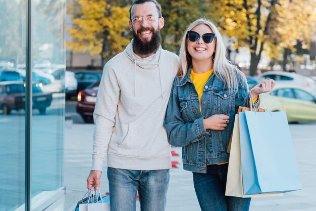 Shopaholics lifestyle Happy couple standing with packages in city center Blur fall landscape background