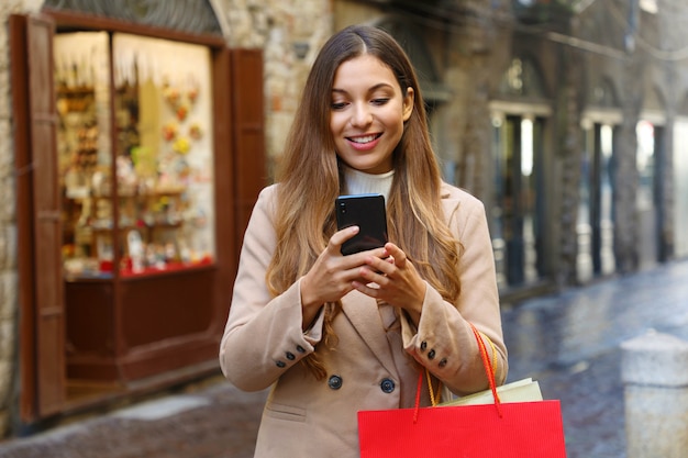 Shopper woman buying online with smart phone in old city street in winter.