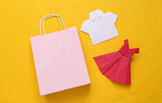 Shopping bag with origami dress and shirt on a yellow background Shopping concept