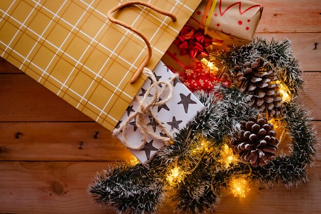 Shopping bag on wooden table with Christmas gift boxes and decorations with yellow lights Preparation for holidays