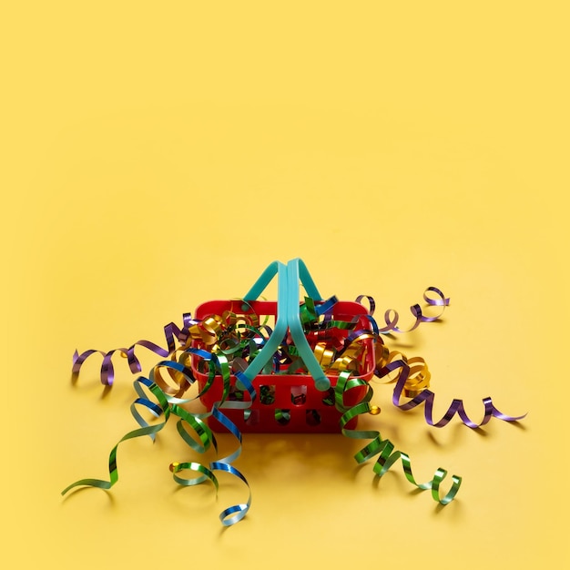 Shopping basket with spirals of tinsel and bag on top on a colored background Copy space