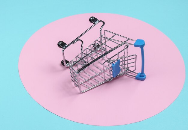 Shopping cart on blue background with pink pastel circle. Minimalistic shopping concept, shopaholic.