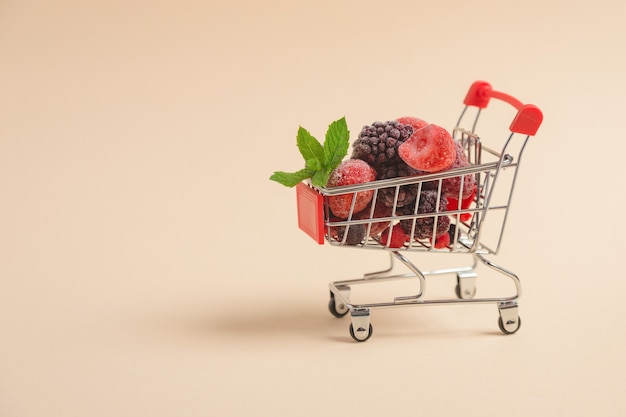 A shopping cart filled with frozen berries on a beige surface with space for text