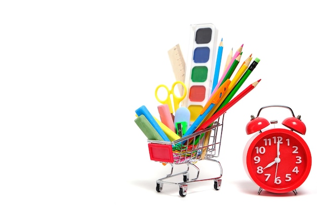 Shopping cart full school supplies and office supplies and red alarm clock white background