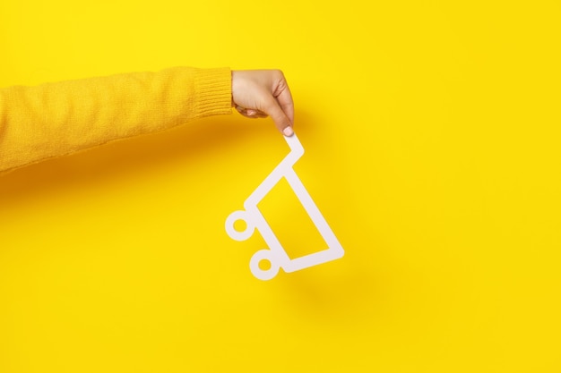 Shopping cart in hand over yellow background