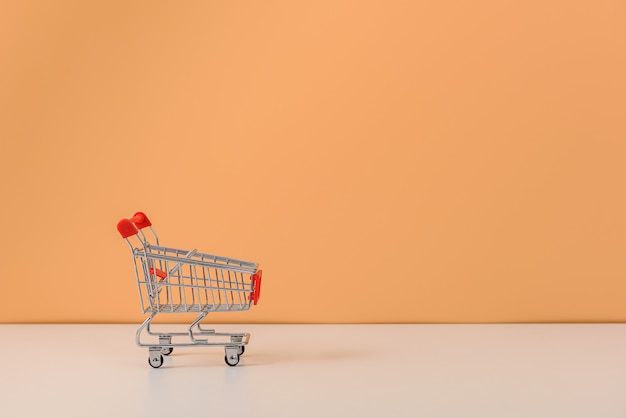 Shopping cart or trolley on white table and pastel orange