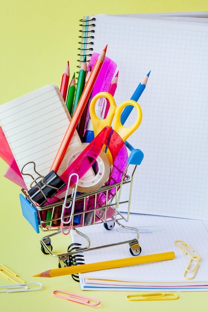 Shopping cart with different stationery on the yellow background