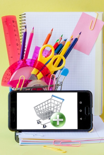 Shopping cart with different stationery on the yellow background