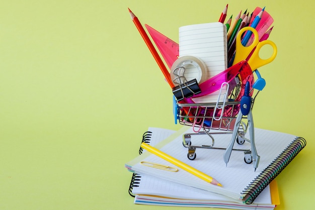 Shopping cart with different stationery on the yellow background