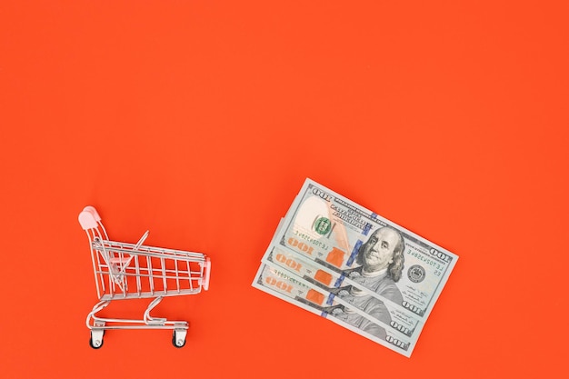 Shopping cart with dollar banknotes on a red backgroundBusiness finance shopping conceptSaving currency Investments Copy space