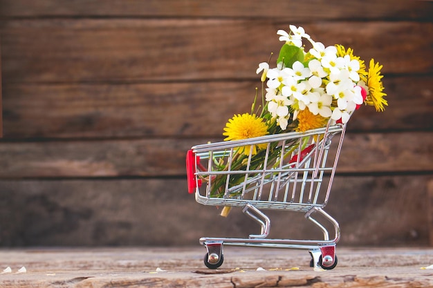 Shopping cart with flowers on the wooden background Toned image