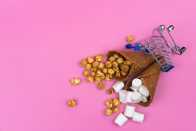 Shopping cart with ice cream cones on a pink background