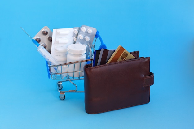 A shopping cart with pills, and syringe next to a purse with credit cards 