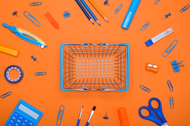 shopping cart with school supplies on orange background