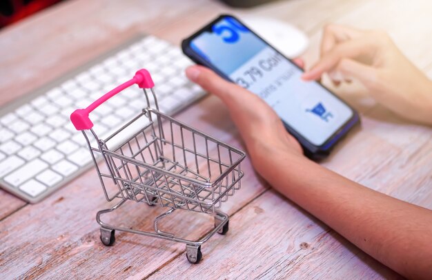 shopping cart on wooden table Behind a woman using a blurry smartphone online shopping