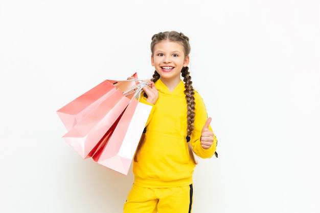 Shopping for children A beautiful little girl in a yellow sports suit holds paper shopping bags on a white isolated background