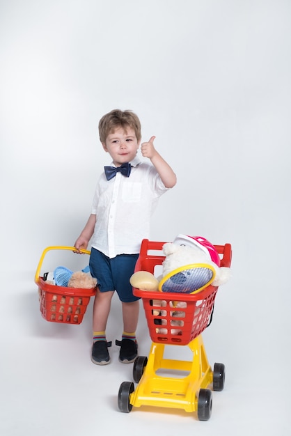 Shopping concept child with shopping basket and shopping cart giving thumb up toddler boy with child