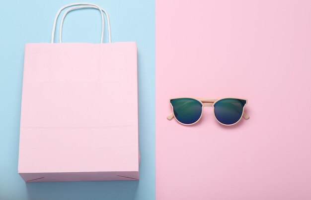 Photo shopping concept paper shopping bag with sunglasses on bluepink pastel background flat lay