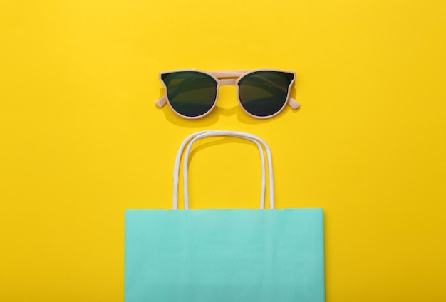 Photo shopping concept paper shopping bag with sunglasses on yellow bright background flat lay